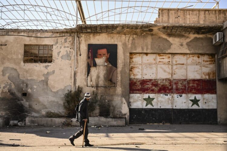 A man walks past a defaced portrait of ousted president Bashar al-Assad is pictured in the town of Adra on the northeast outskirts of Damascus on December 16, 2024. Islamist-led rebels took Damascus in a lightning offensive on December 8, ousting president Bashar al-Assad and ending five decades of Baath rule in Syria. (Photo by Aris MESSINIS / AFP)