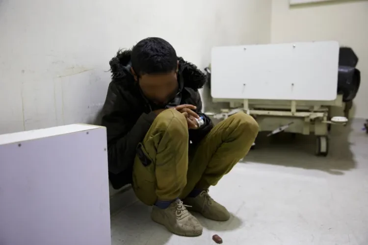 Crouching on the floor of a hospital room, this man does not know who he is any more after the torture he lived through [Ali Haj Suleiman/Al Jazeera]