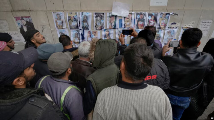 FILE - People examine photos as they search for missing or deceased people on the wall outside the morgue of Al-Mojtahed Hospital in Damascus, Syria, Dec. 11, 2024.